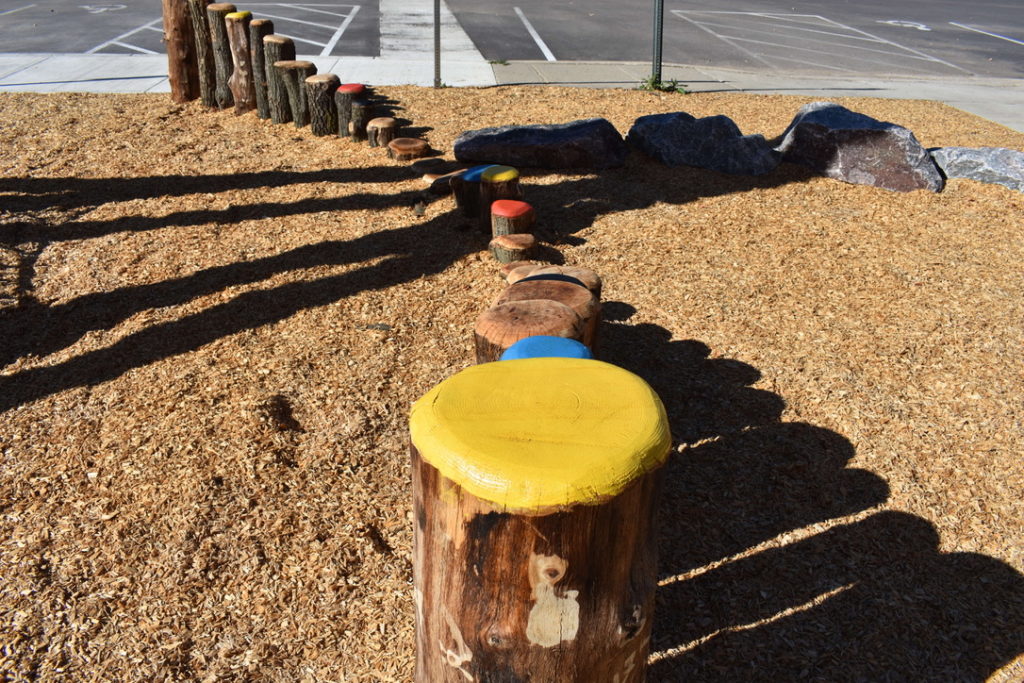 A descending then ascending row of wood stumps with yellow, blue, and red painted tops