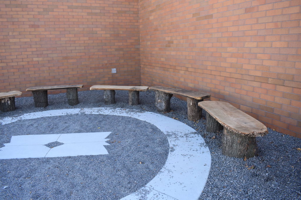 Wooden benches in a semi-circle around a customized concrete design on the ground